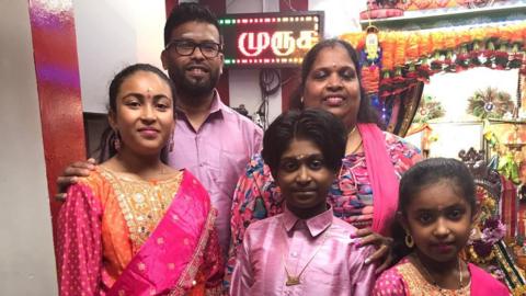 A family dressed ready for the Hindu celebration of Diwali in bright mostly pink and golden clothes. The parents stand at the back, three children at the front  