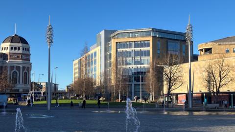 A large eight-floor office building with big glass windows viewed from Bradford's City Park.