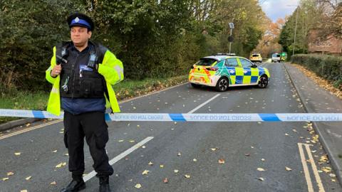 A police officer standing in front of a police cordon on the road where the incident happened in Lawrence Weston