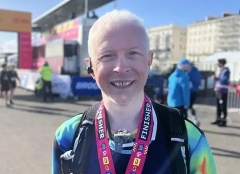 A man with short white hair wearing a running top smiles towards the camera