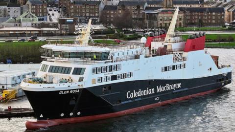 A large ferry moored at a quayside. Caledonian MacBrayne is written on the side with the name Glen Rosa at the front. The ship is black and white with red funnels