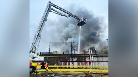 An aerial arm over lots of smoke with a hose firing water below