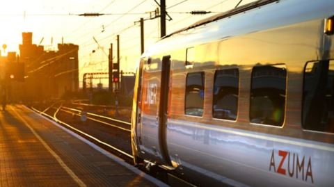 A red and grey LNER train departing Newcastle train station at sunrise. Newcastle Castle could be seen in the distance. 