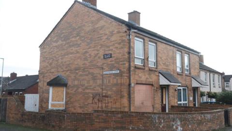 The house which was attacked at Glenrosa Link, north Belfast.  The ground floor windows of the semi-detached, brown brick house are boarded up and there is graffiti on the side of the building. 