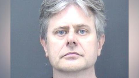 A mug shot of a man with medium-length grey/white hair.