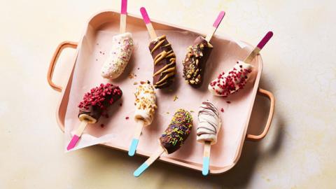 Frozen banana lollies dipped in chocolate and topped with various toppings.