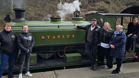 Representatives of organisations leading Stanley's Town of Culture bid stand in front of a green steam train with the word Stanley printed on the side.