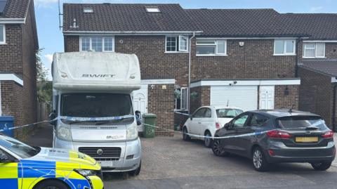 A general view of a two-storey semi-detatched house with a campervan and two cars parked on a driveway.