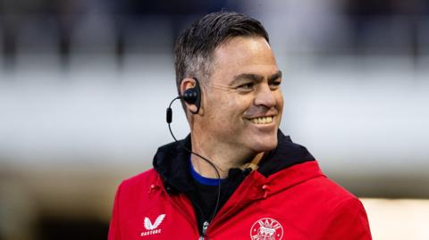 Johann van Graan walking on the pitch looking over his left shoulder while smiling