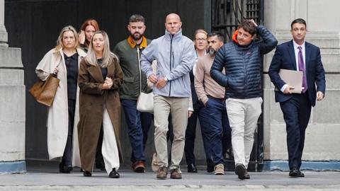 The families of the three girls killed in the Southport attack walk towards Liverpool Town Hall, with their legal representative beside them