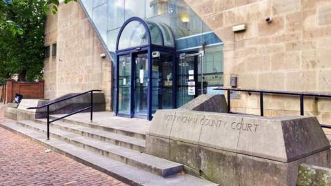 The exterior of Nottingham Crown Court which is a light brick building with a glass frontage and blue-framed glass doors.