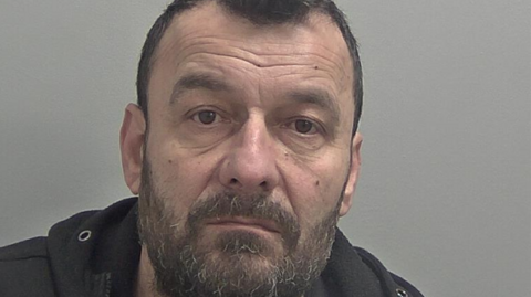 Police mugshot of Arian Varfaj who has a beard and short dark hair