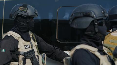 Two government forces personnel wearing all black and beige vests.