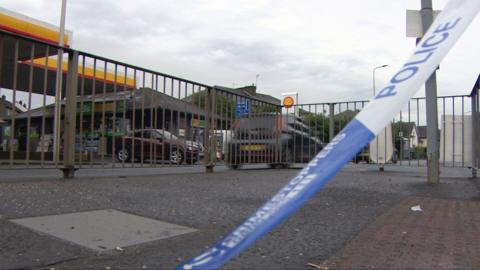 A garage forecourt with a police blue and white banner draped across it.