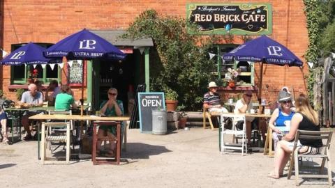 People sitting at tables in front of the Red Brick Cafe on a sunny day.
