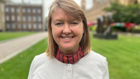 Sarah Gibson looking at the camera smiling outside the Houses of Parliament