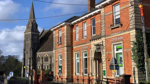 Lloyds Bank in Gillingham was housed in an older two-storey red brick building with large windows and an ornate pillar on the side.