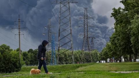 A woman walks in a park as smoke billows in the background following a reported Ukrainian drone attack, in Moscow, Russia, 18 June 2026.