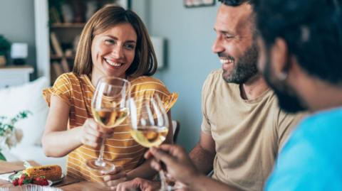 A group of friends drinking white wine from glasses while sitting down to eat a meal.