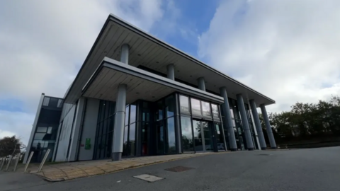 A modern further education college building with large glass windows and a grey plastic-clad  facade.