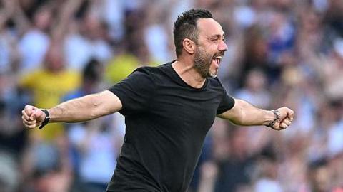 Roberto de Zerbi celebrates with a broad smile and arms outstretched as he runs on to the pitch in a black T-shirt