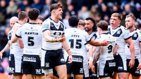 Hull FC players, in their white shorts and black shorts, celebrate a try against Catalans Dragons, with Davy Litten in the foreground urging the crowd to increase their support.