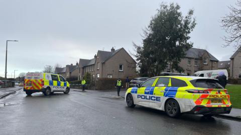 Two police vehicles in front of a cordon on Drum Brae Drive in Edinburgh.