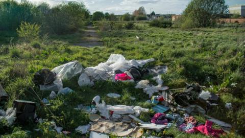 Clothing and other garbage dumped on overgrown site of demolished housing estate