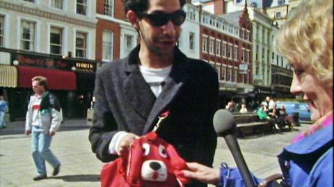 A man in St Ann's Square, Manchester showing Esther Rantzen his dog-shaped handbag.