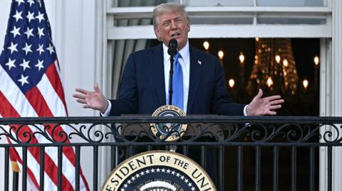 Donald Trump stands on a balcony outside the White House