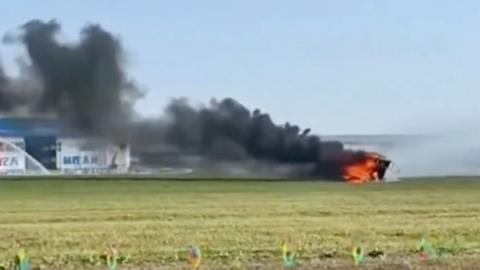 A still from a video of a flaming flying car crash. Black smoke is blowing to the left.