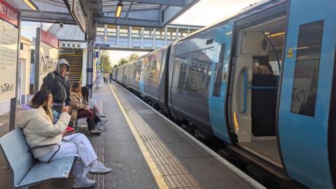 A blue Southeastern Railway train arriving at Canterbury West station platform with passengers waiting.