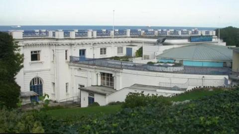 Top shot of large white Edwardian building cut in the cliffs with sea behind
