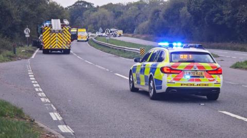 A police car is parked on an motorway with fire engines further down the road