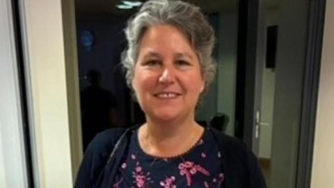 Julie Conlen who won the award, smiling at the camera. She is wearing a black and pink patterned top and black cardigan. 