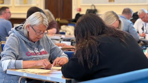 People sit at a table counting votes cast during the 2026 Jersey general election.