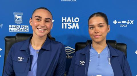 Two women in Ipswich Town gear smiling at the camera at a press conference.