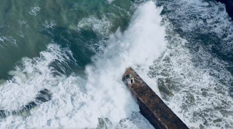 Aerial views of large waves crashing over a pier.