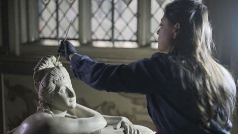 A woman works on a statue 