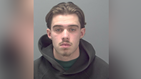 A mugshot of a young man wearing a hooded top