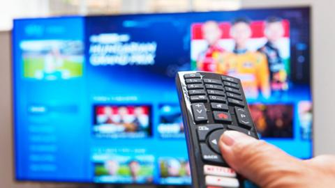 Close up of a person holding a TV remote, pointing at a smart TV