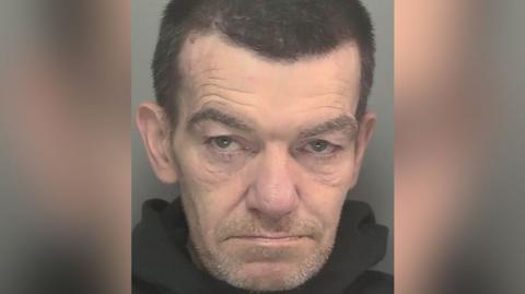 Undated handout custody photo issued by Merseyside Police of Steven Wales. He has dark brown hair and grey stubble.