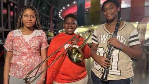 Eliannah, 13, Isaiah, 12, and Etania, 14, holding musical instruments at the Glasshouse. 