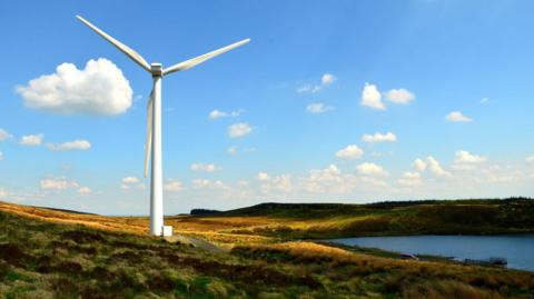 A solo windmill on a grassy area beside a lake in an unknown area of Northern Ireland 