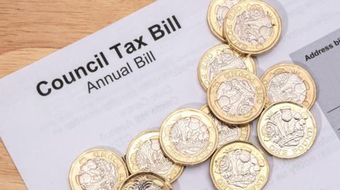 A council tax bill close up on a table with pound coins on top of it. 