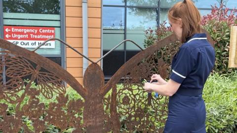 Afton Cope, a woman, wearing a blue uniform tying a blue ribbon to the brown sculpture. 