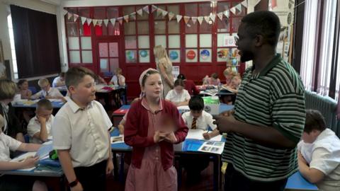 De-Graft speaking to two children in a classroom.