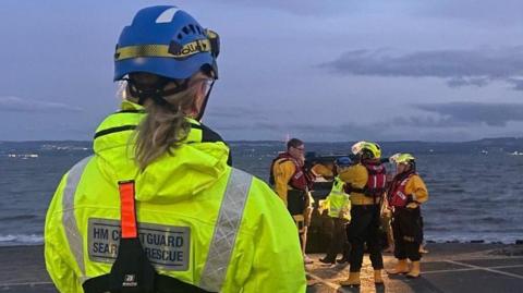 A woman in wearing a high visibility yellow jack with HM Coastguard Search and rescue written on the back.