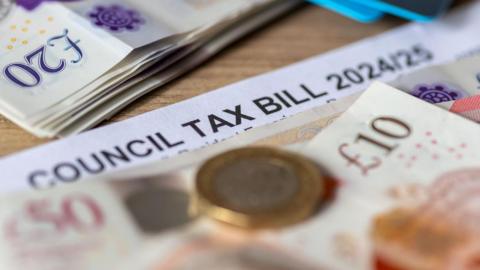 A table with £20, £50 and £10 notes and a £1 coin on it. A piece of paper is underneath, with "Council tax bill 2024/25" as the heading.