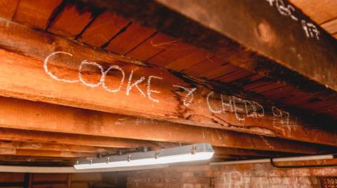 A large wooden beam on a roof with the words "Cooke and Chedd 97" written on it.